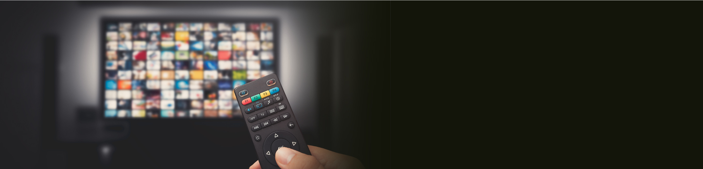 TV screen blurred in background with hand holding remote in foreground